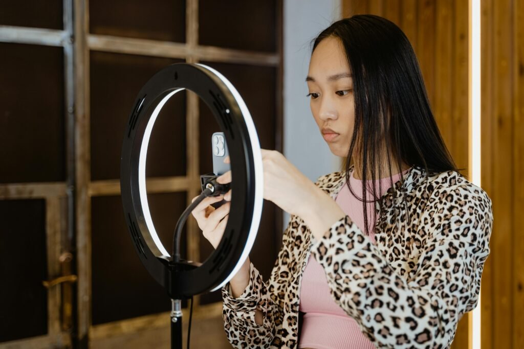 pexels-photo-7481984-7481984 Asian woman with leopard print jacket adjusts ring light for smartphone streaming setup.